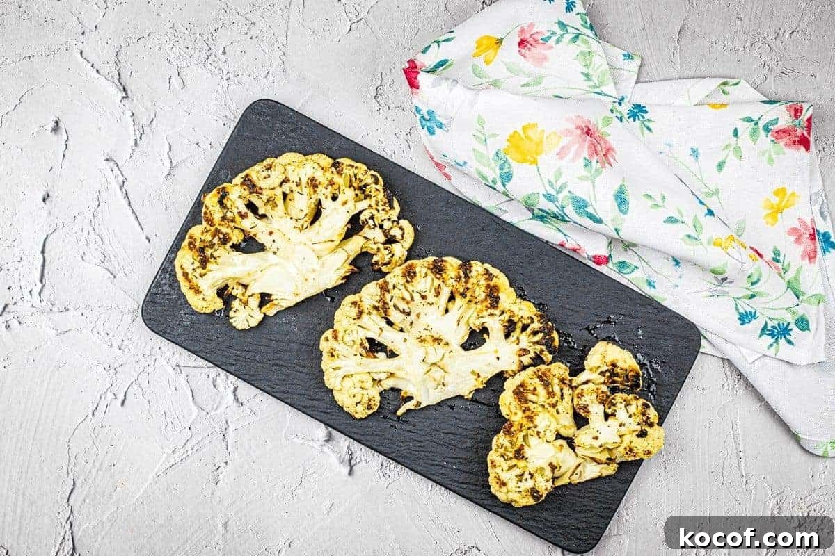 39 Outdoor Grilling Dinners That Make You Ditch the Oven Tonight 11 Three pieces of grilled cauliflower steaks on a black plate.