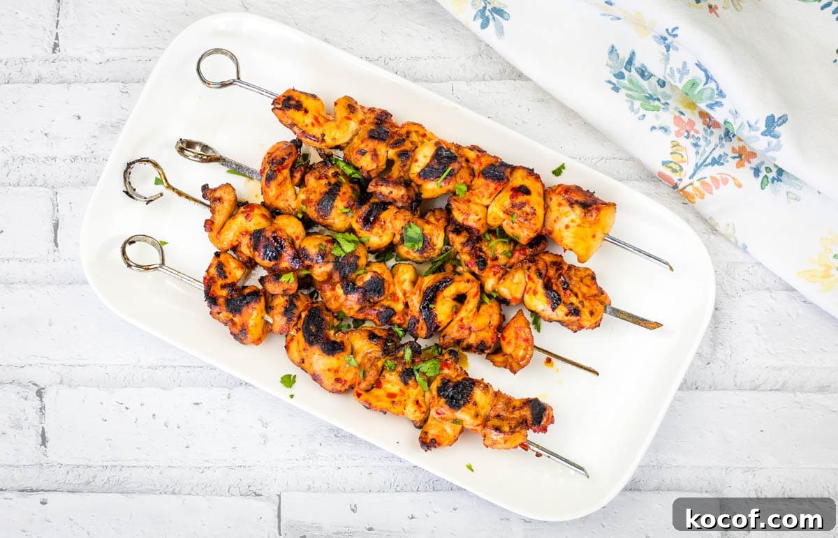 39 Outdoor Grilling Dinners That Make You Ditch the Oven Tonight 15 A rectangular white plate with four Sweet & Spicy Grilled Harissa-Honey Chicken Skewers garnished with chopped herbs.