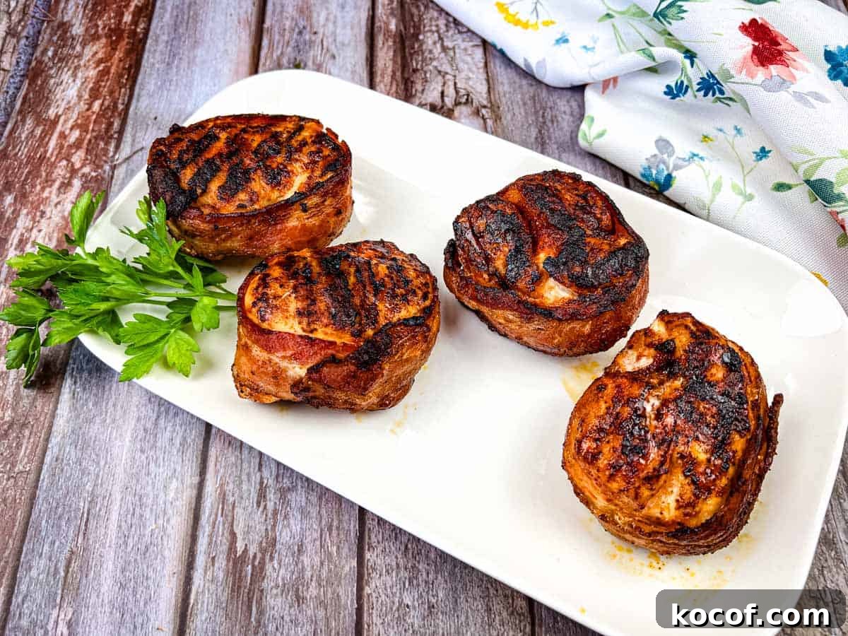 39 Outdoor Grilling Dinners That Make You Ditch the Oven Tonight 20 Four bacon-wrapped chicken breasts on a white rectangular plate garnished with sprigs of parsley.