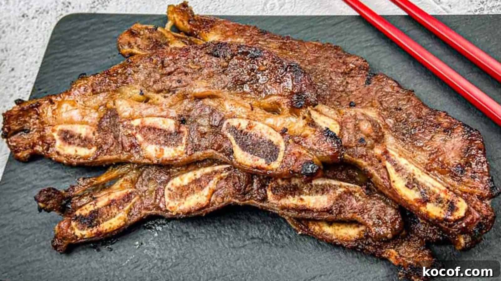 39 Outdoor Grilling Dinners That Make You Ditch the Oven Tonight 3 Korean Galbi Ribs on a slate platter with red chopsticks beside them.
