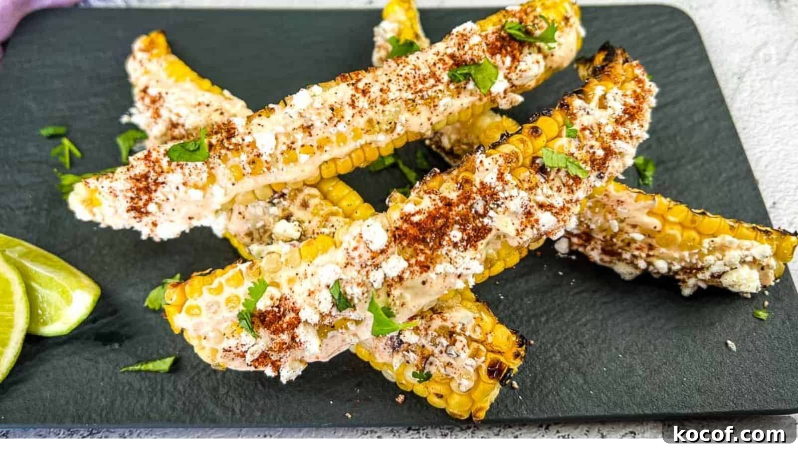 39 Outdoor Grilling Dinners That Make You Ditch the Oven Tonight 26 Grilled corn on the cob pieces topped with cheese, chili powder, and cilantro, served on a black slate plate with lime wedges on the side.