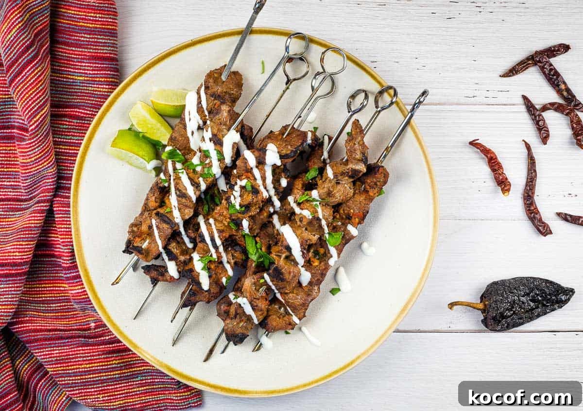 39 Outdoor Grilling Dinners That Make You Ditch the Oven Tonight 31 Grilled Steak skewers on a white plate with chilis nearby.