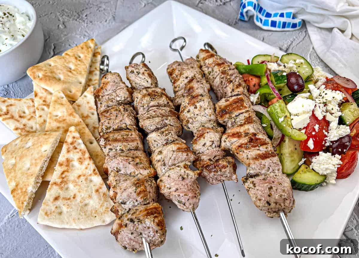 39 Outdoor Grilling Dinners That Make You Ditch the Oven Tonight 10 Ninja Woodfire Pork Souvlaki with Horiatiki Salad and pita bread on a white plate.