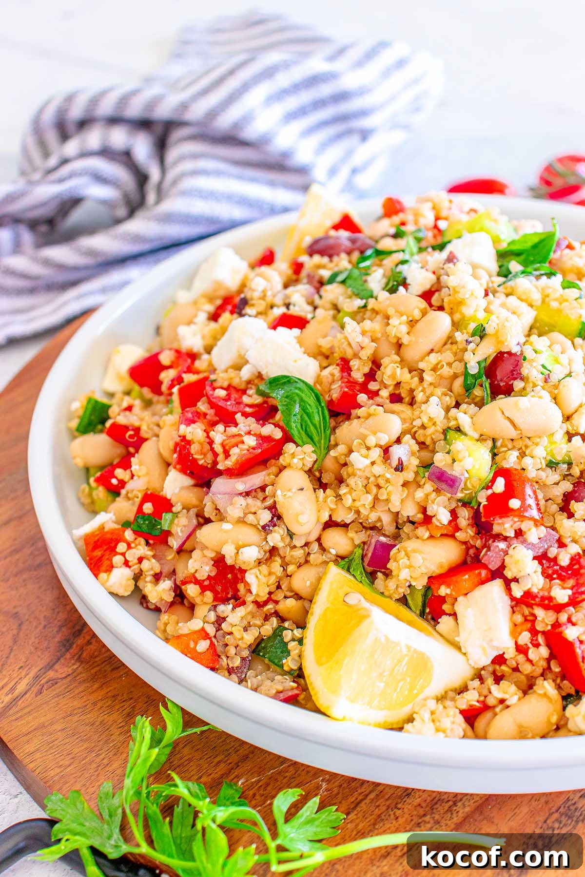 Mediterranean Quinoa Salad with Feta, Cucumbers & Olives 11 A bowl of Mediterranean Quinoa Salad with beans, tomatoes, feta, fresh herbs, and a lemon wedge is served on a wooden tray.