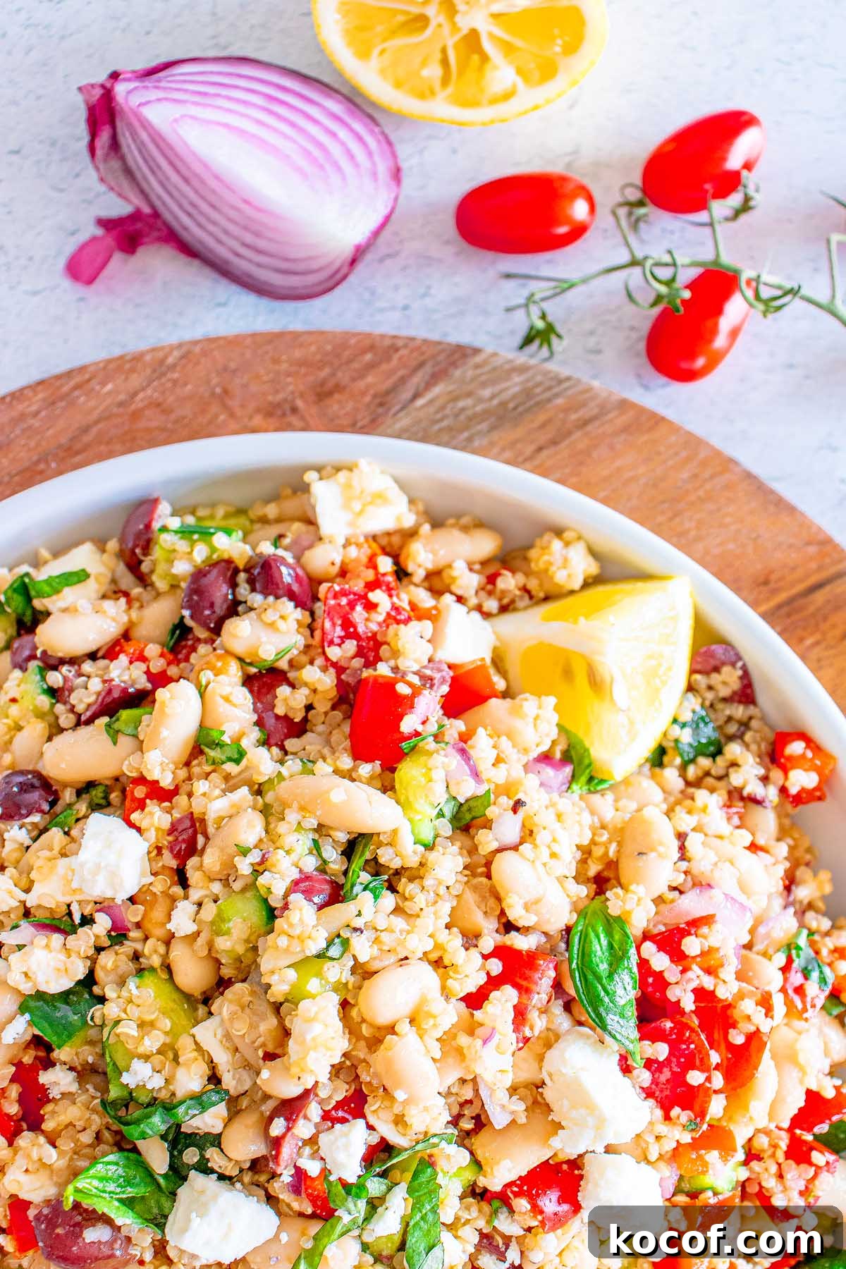 Mediterranean Quinoa Salad with Feta, Cucumbers & Olives 4 A bowl of Mediterranean Quinoa Salad with feta, beans, tomatoes, olives, and lemon, surrounded by fresh veggies.