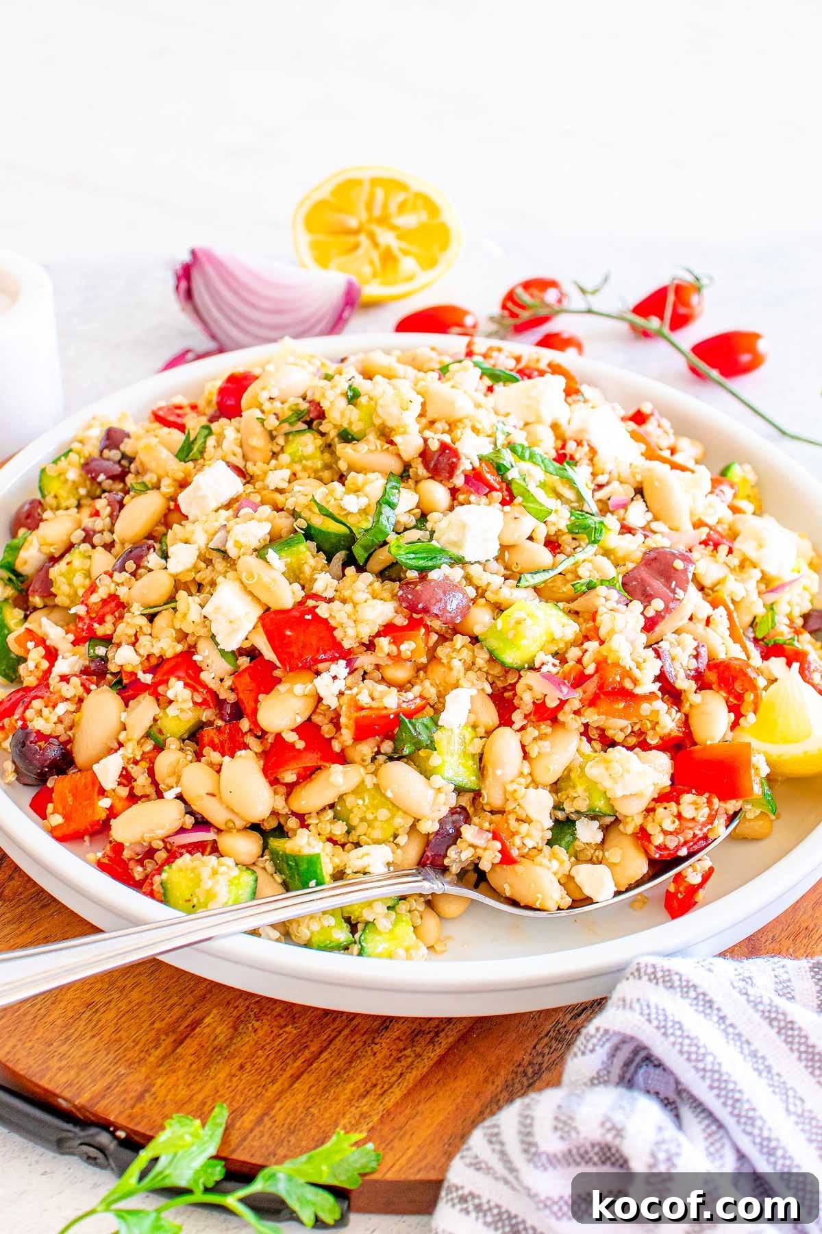 Mediterranean Quinoa Salad with Feta, Cucumbers & Olives 7 A bowl of vibrant Mediterranean Quinoa Salad with beans, feta, cucumber, tomatoes, olives, and fresh herbs on a white plate.
