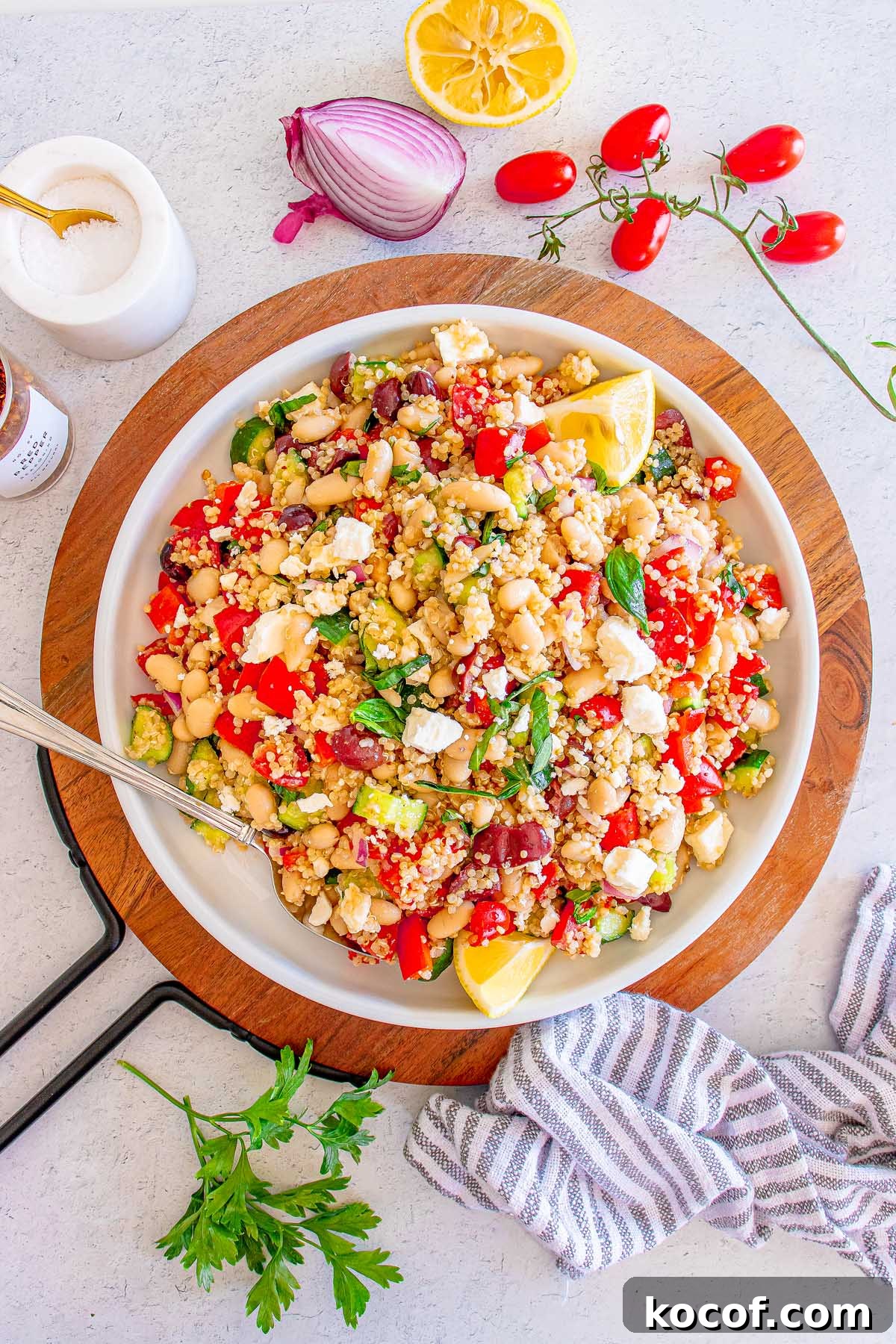 Mediterranean Quinoa Salad with Feta, Cucumbers & Olives 9 A vibrant Mediterranean Quinoa Salad featuring chickpeas, tomatoes, feta, lemon wedges, and fresh herbs is beautifully arranged in a bowl on a rustic wooden board.