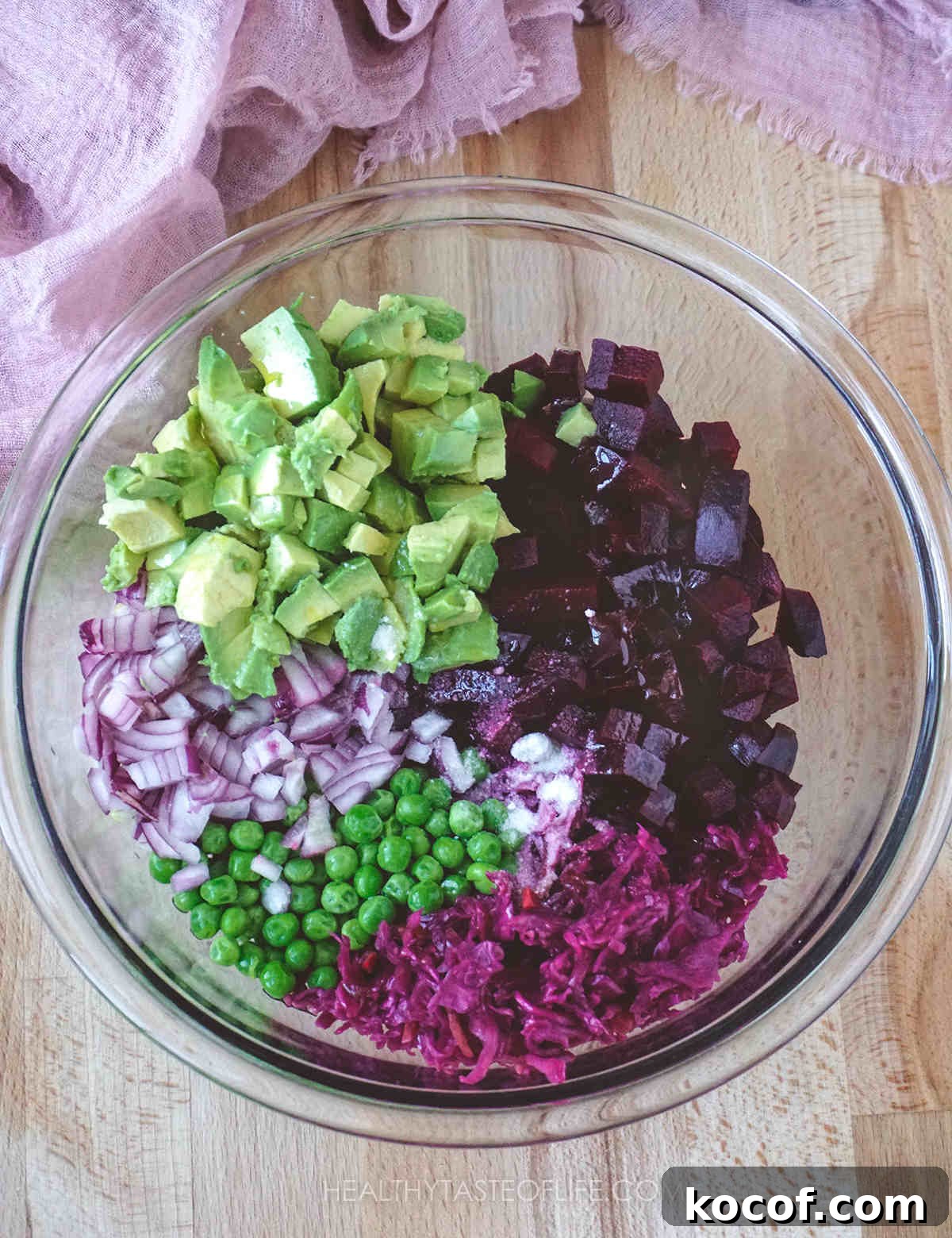 Russian Vinaigrette Salad with Beets and Sauerkraut 5 Process shot showing diced beets, onion, peas, sauerkraut, avocado and vinaigrette all arranged in a glass bowl, ready to mix and finish the Russian beet salad.