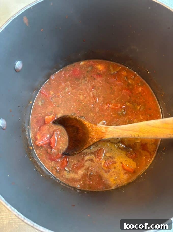 overhead image of nonstick pot cooking chunky tomato soup with a wooden spoon