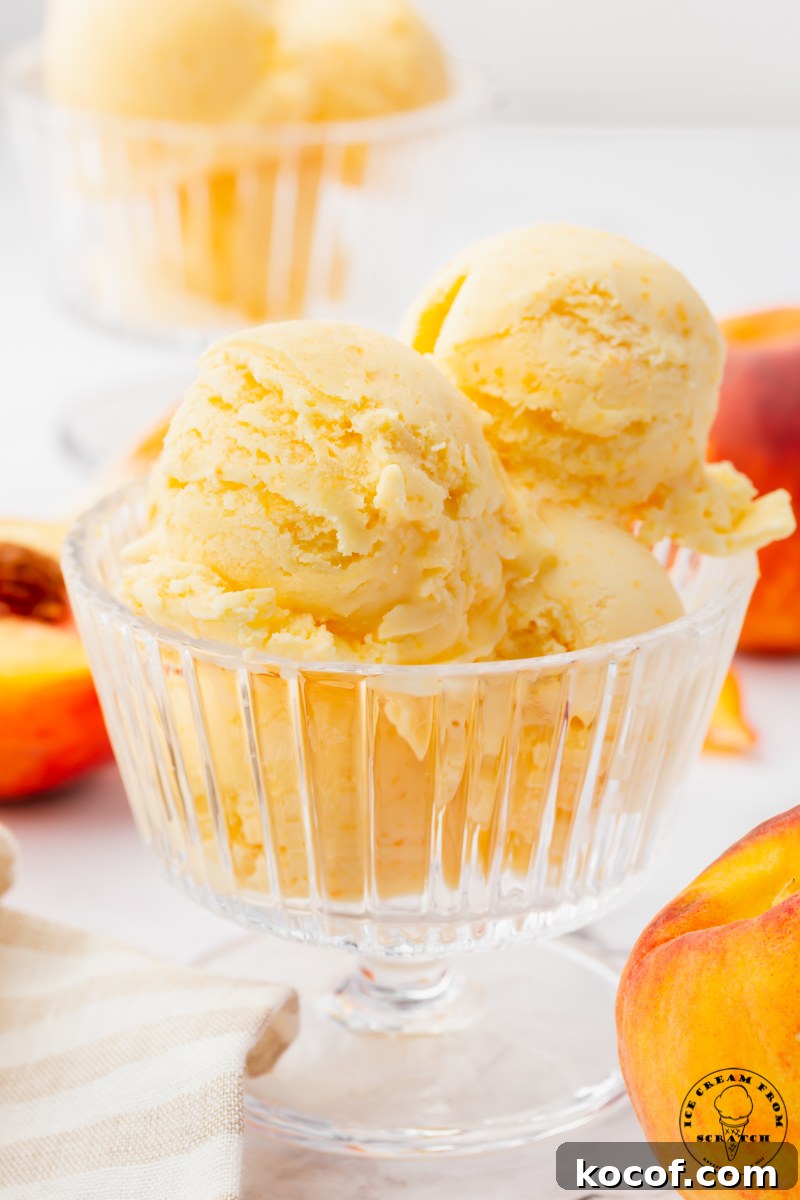 a footed glass ice cream dish filled with 4 scoops of fresh peach ice cream. Peaches are in the background.