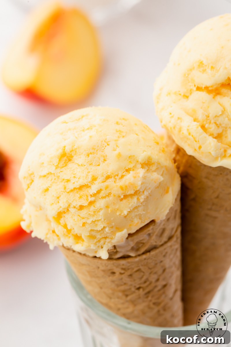 two sugar cones topped with a scoop of fresh peach ice cream, propped up in a glass.