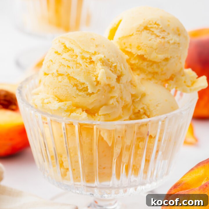 a footed glass ice cream dish filled with 4 scoops of fresh peach ice cream. Peaches are in the background.