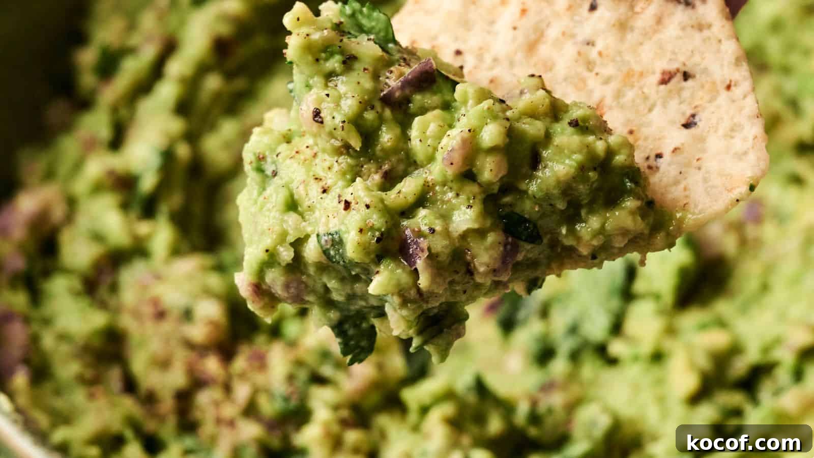 Close-up of guacamole on a tortilla chip, showing a textured mixture of avocado, herbs, and spices.