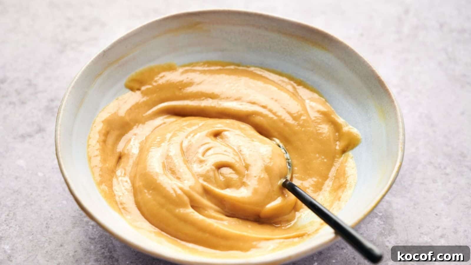 A bowl of smooth, creamy peanut butter with a hint of Chick-fil-A sauce and a spoon inside.