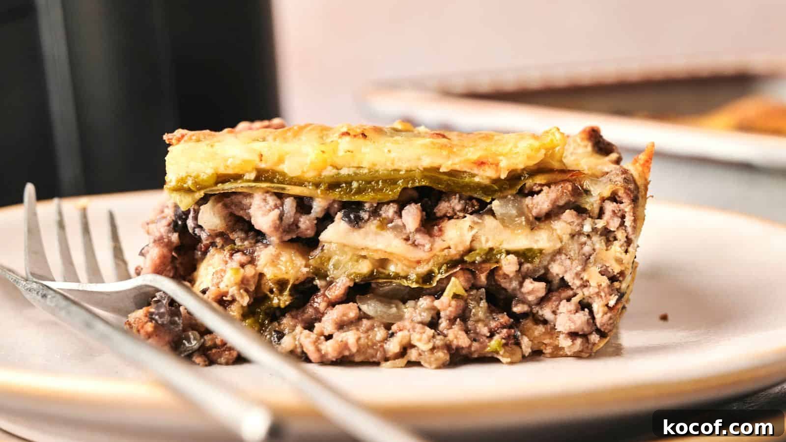 Close-up of a slice of layered casserole with ground meat, cheese, and vegetables on a plate with a fork.