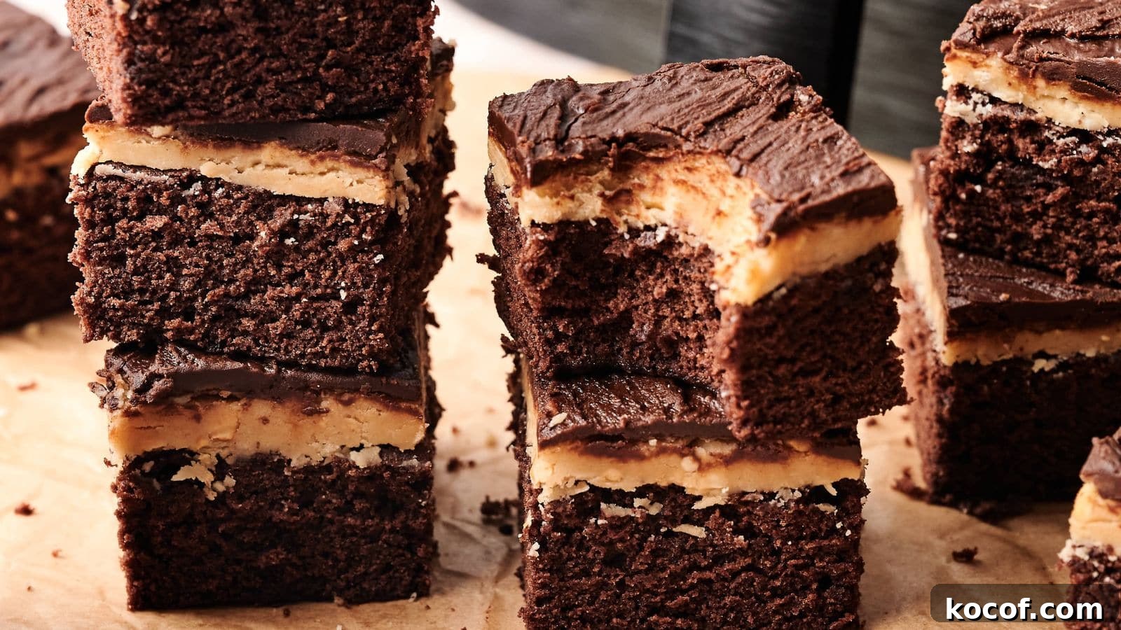 Several stacked chocolate brownies with a layer of peanut butter filling and chocolate frosting, placed on a parchment-covered surface.