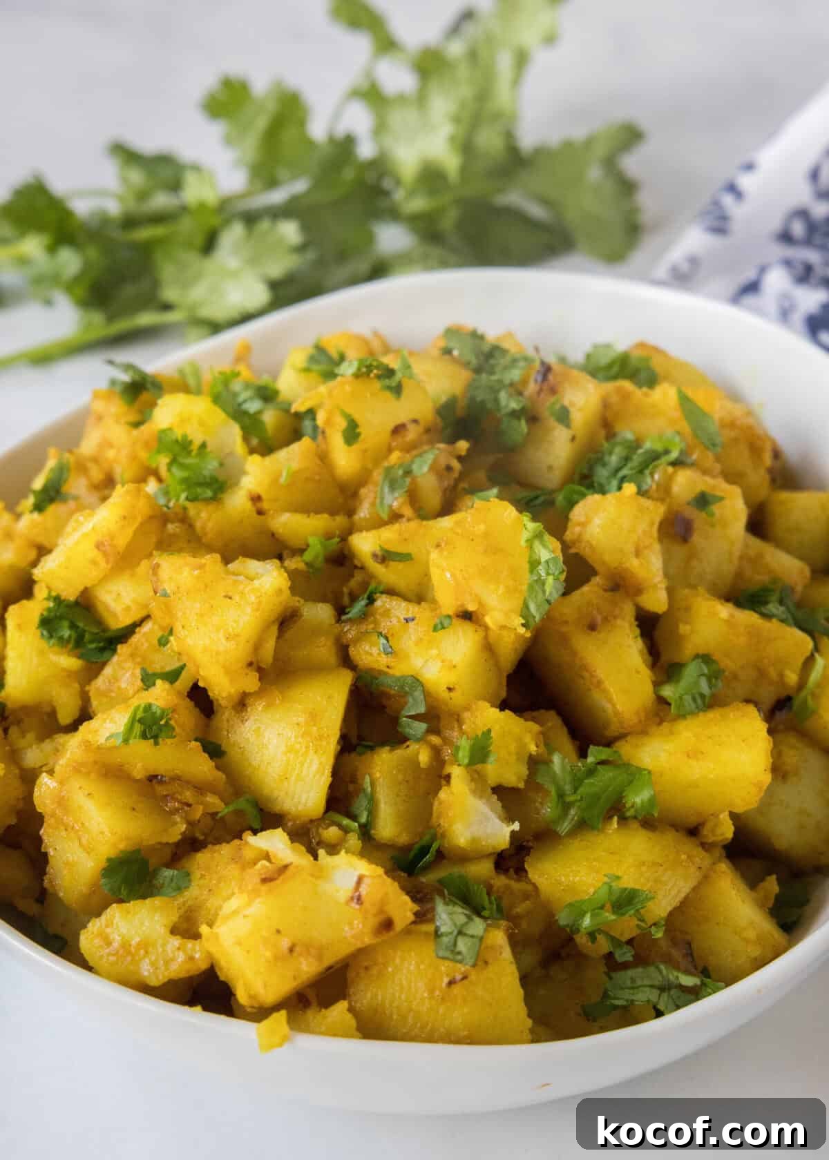 a serving bowl with curried potatoes topped with cilantro