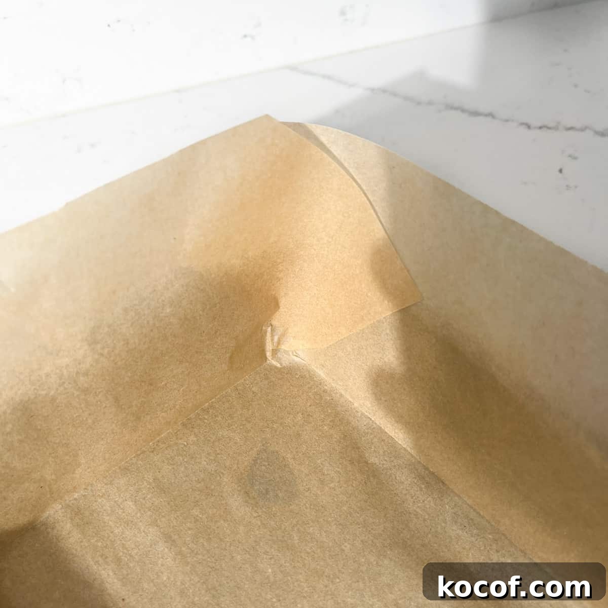 Overlapping corners of baking paper lining a baking tin.