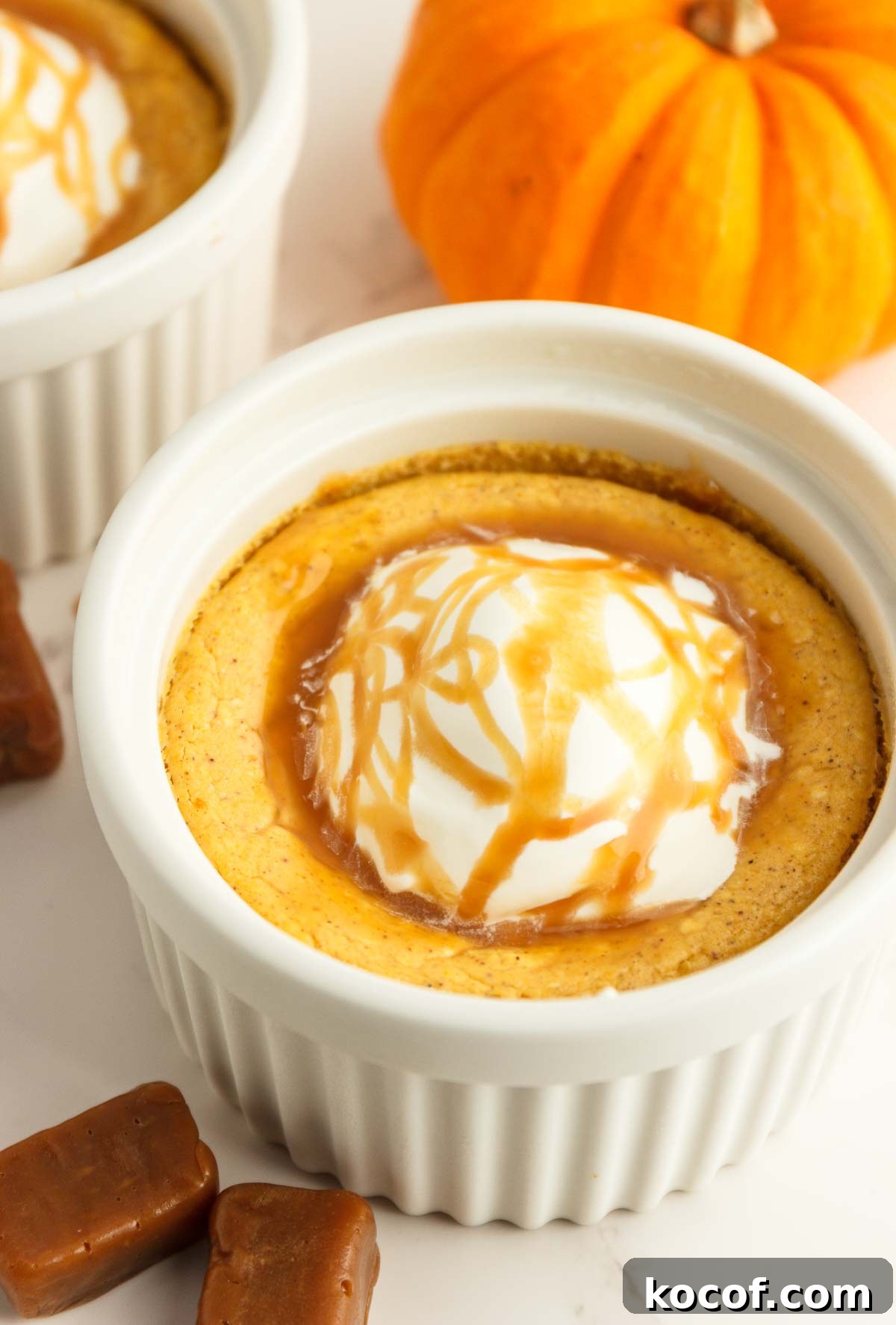 Two easy keto pumpkin cheesecakes in white ramekins with whipped cream and caramel syrup.