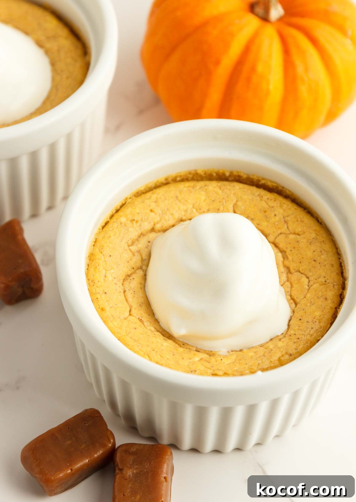 Two easy keto pumpkin cheesecakes in white ramekins with whipped cream.