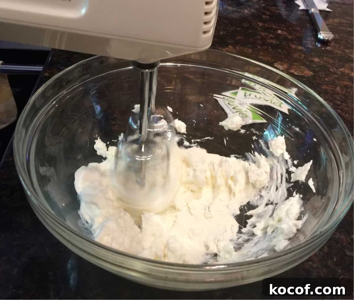 Beating cream cheese and sweetener in glass bowl with hand mixer.