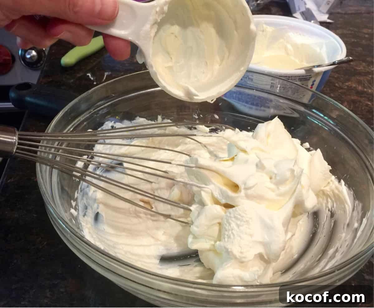 Whisking greek yogurt, vanilla and lemon juice into sweetened cream cheese mixture.