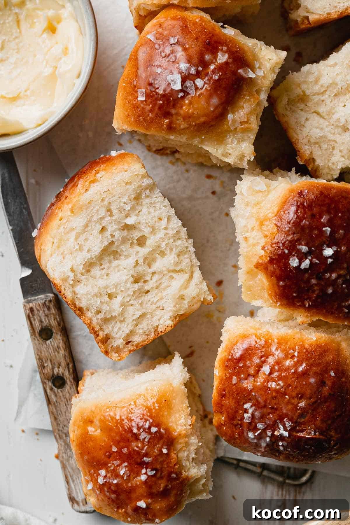 Fluffy gluten-free dinner rolls on parchment, one on side showing airy texture.