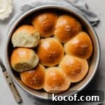 Baked gluten-free pull-apart dinner rolls in a round pan, one roll pulled apart to show the fluffy interior.