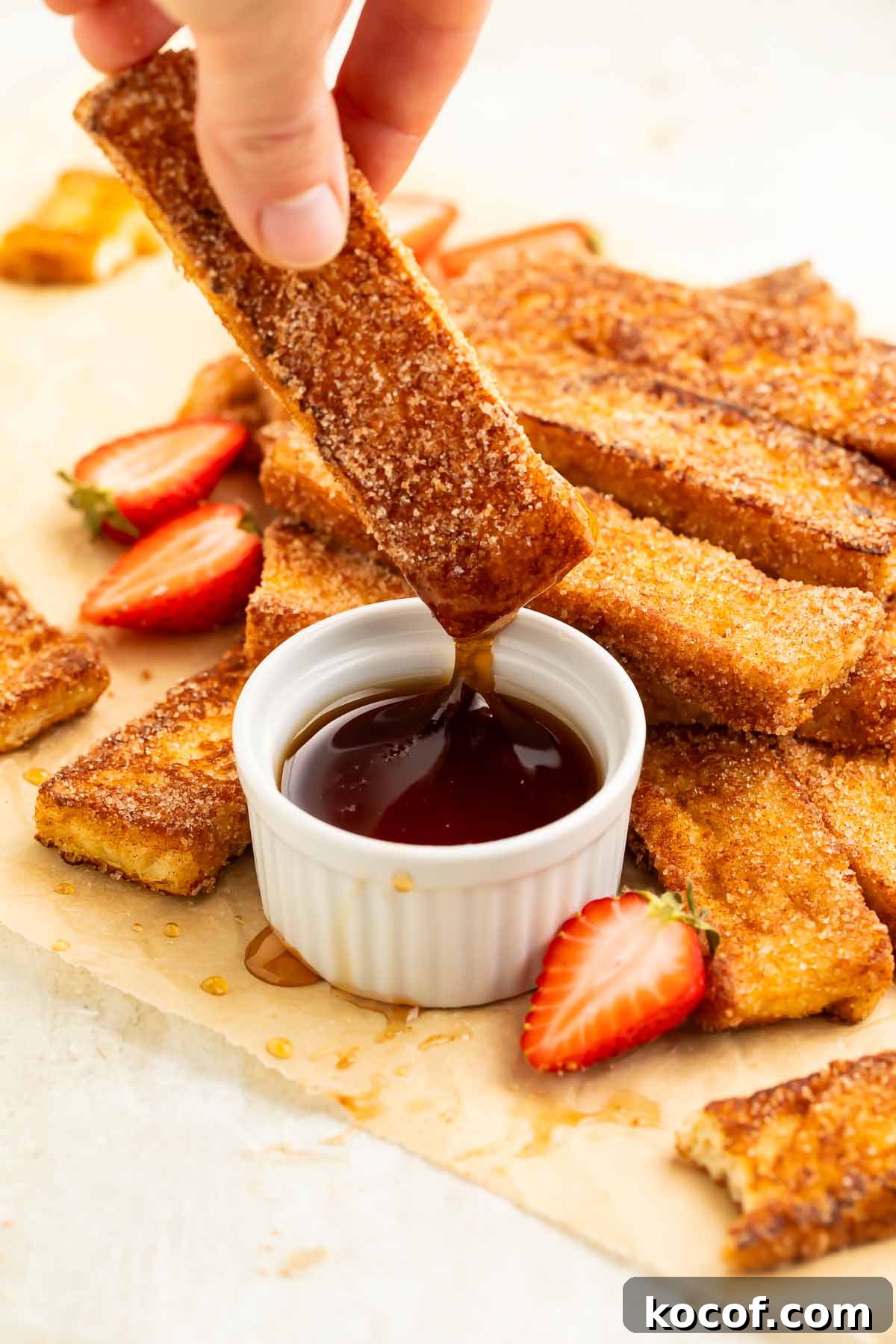 A keto french toast stick being dipped into and lifted out of a ramekin of keto maple syrup.