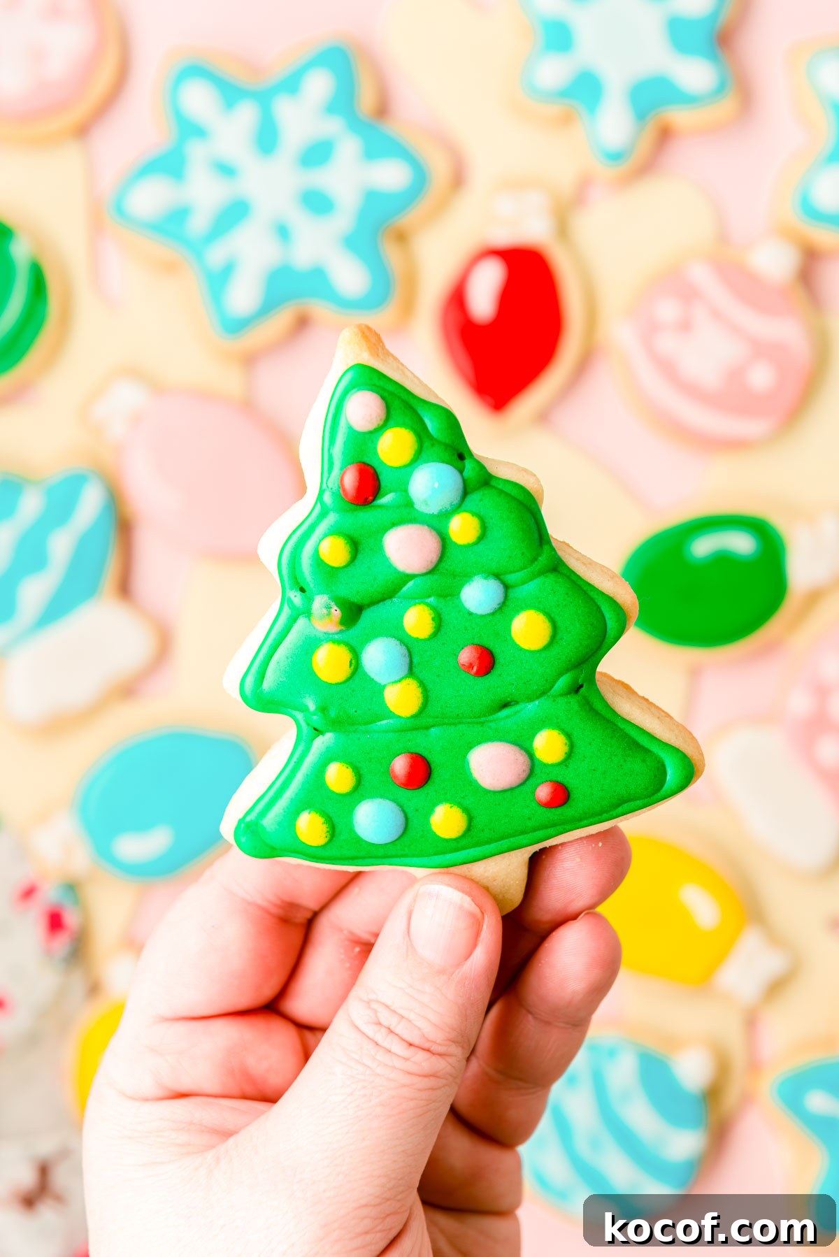 A woman's hand holing an iced Christmas tree cookie to the camera.
