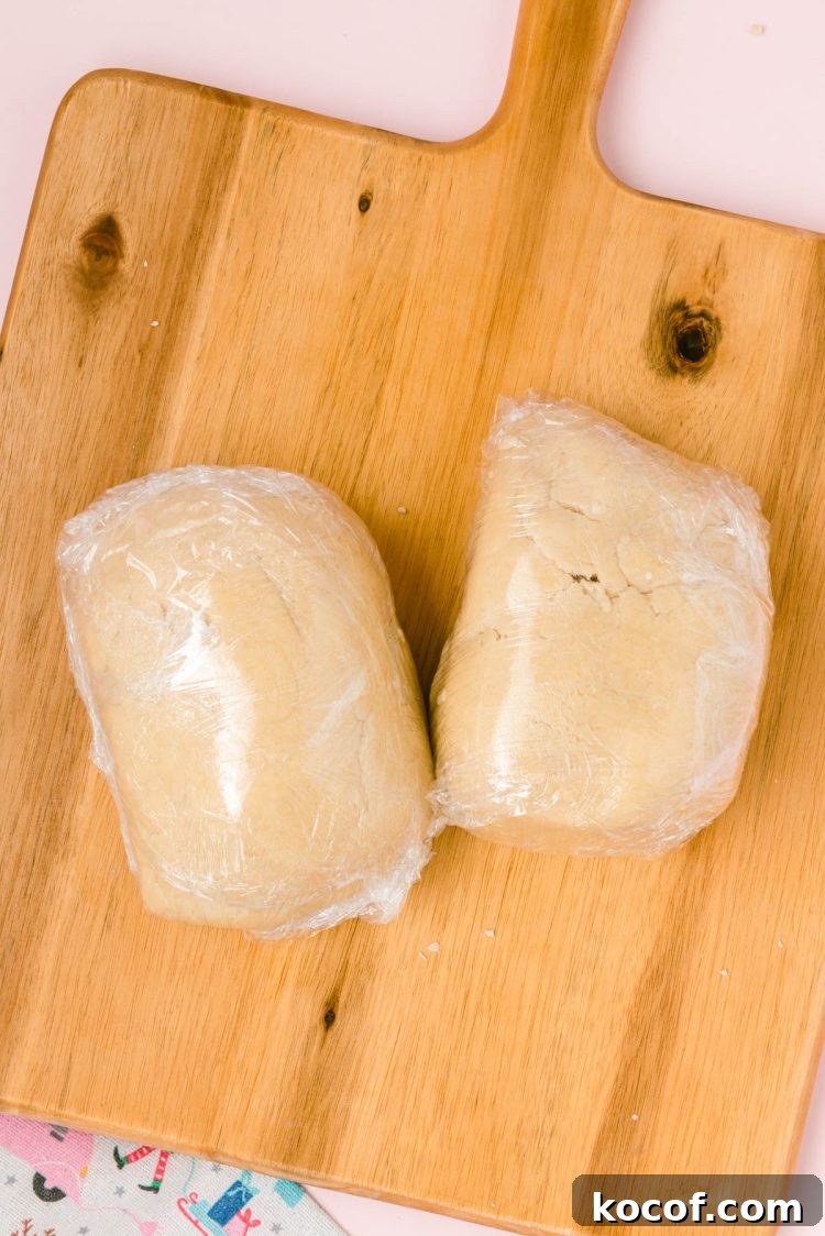 Dough divided into two portions wrapped in plastic wrap on a wooden board.