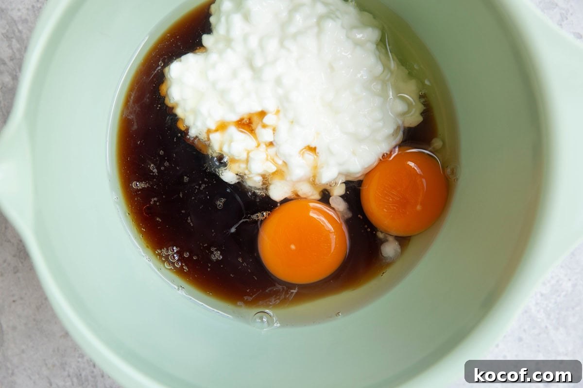 Cottage cheese, pure maple syrup, oil, and eggs in a large mixing bowl, ready to be mixed.