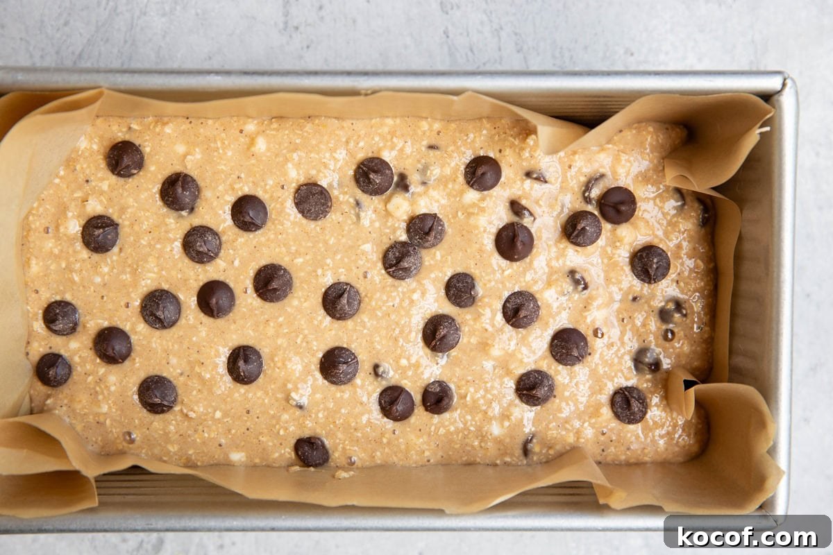 parchment lined loaf pan with chocolate chip bread batter inside, ready to be baked.